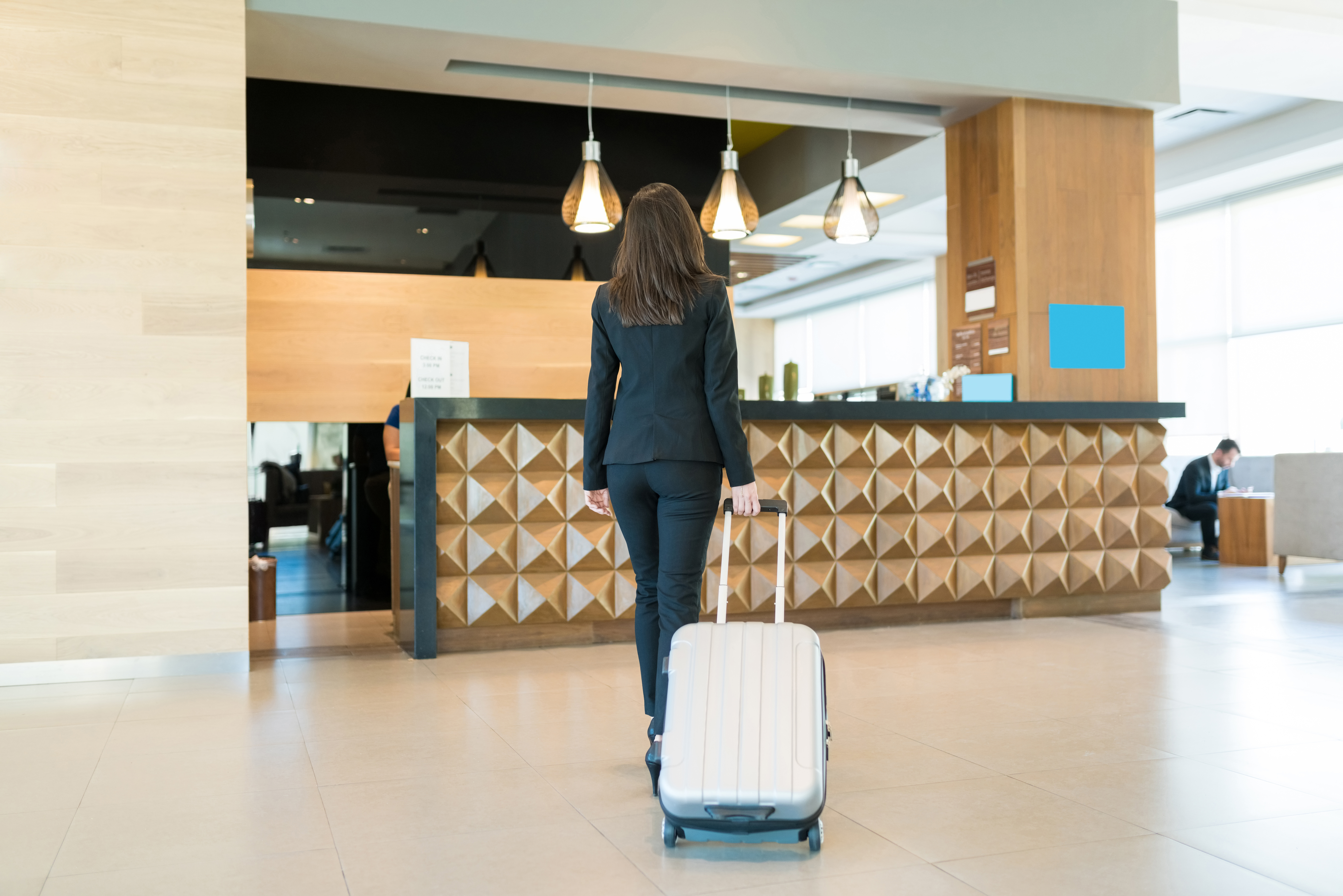 Auf dem Bild ist eine Frau mit einem Koffer in einer Hotel Lobby zu sehen. 